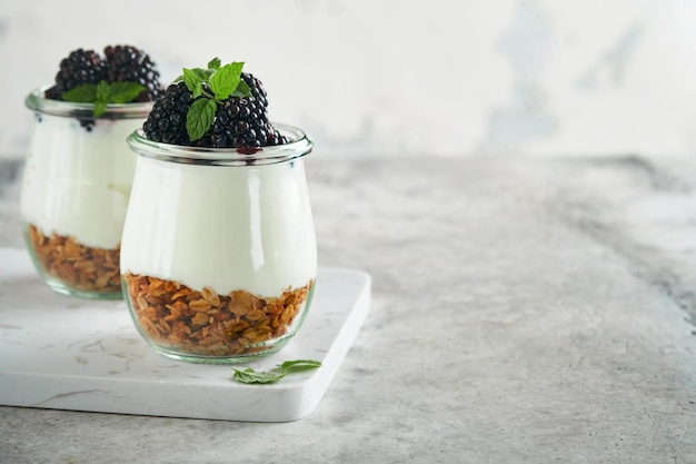 Yogurt with granola blackberry berry fruits and muesli served in glass jar on gray concrete table background Healthy breakfast concept Healthy food for breakfast top view