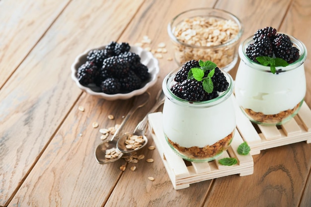 Yogurt with granola blackberry berry fruits and muesli served in glass jar on wooden background Healthy breakfast concept Healthy food for breakfast top view