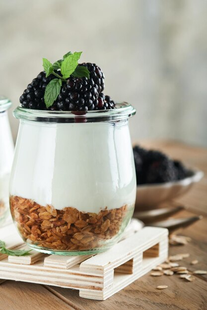 Yogurt with granola blackberry berry fruits and muesli served in glass jar on wooden background Healthy breakfast concept Healthy food for breakfast top view