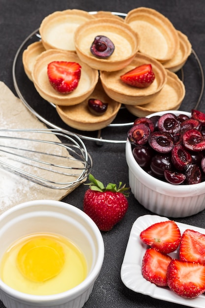 Yolk, Strawberries, sweet cherries and Tartlets with berries on Black background