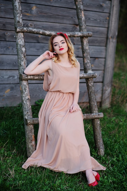 Yong elegant blonde girl at rose dress on the garden background wooden staircase.