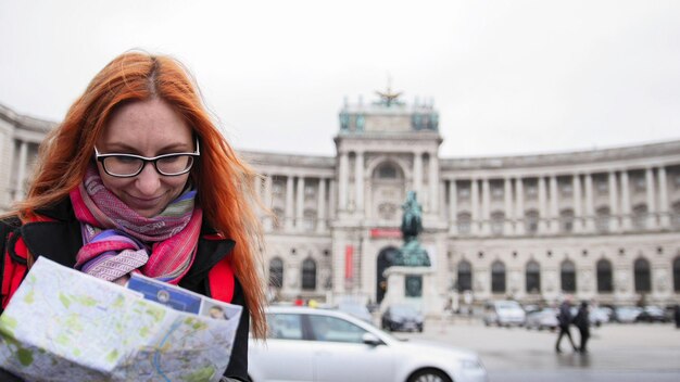 Photo yong tourist - woman with red hair and glasses looking map in heldenplatz, vienna, close up