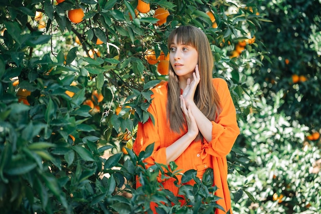 Youg girl in orange dress is posing to camera by looking away in orange garden