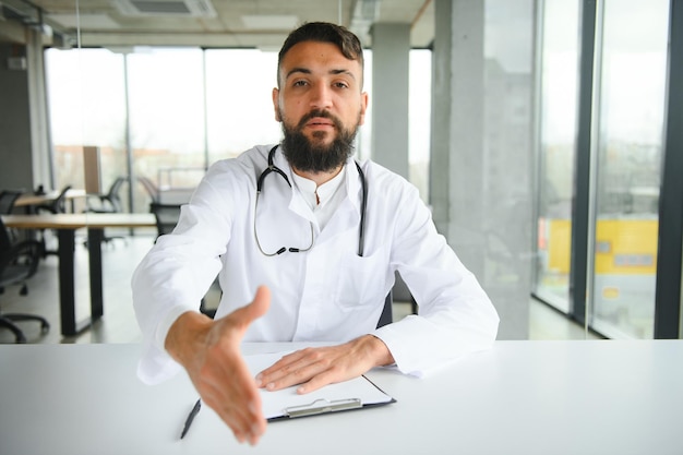 Young 30aged handsome pleasant Arabic male doctor in white coat posing at camera indoors