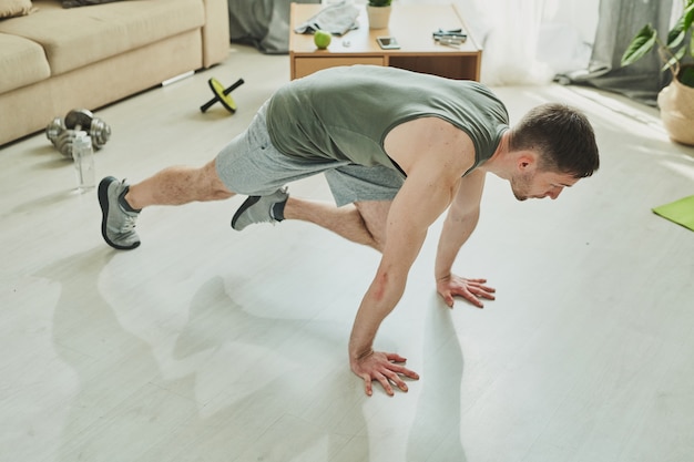 Young active man in sportswear standing on hands and one leg on the floor of living-room while making effort during difficult exercise