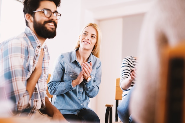 Young addicted people having celebrating situation while sitting together on special group therapy. Handsome hipster guy smiling after his confession and progress.