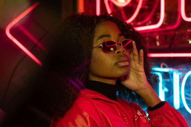 Young adult afroamerican female wearing glasses in front of neon light sign, shallow selective focus