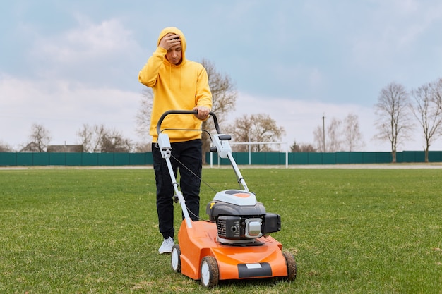 Young adult attractive gardener mows lawn in large field