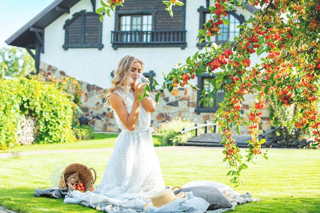 Young adult beautiful blonde in a white dress a wine glass in her hand in the garden under