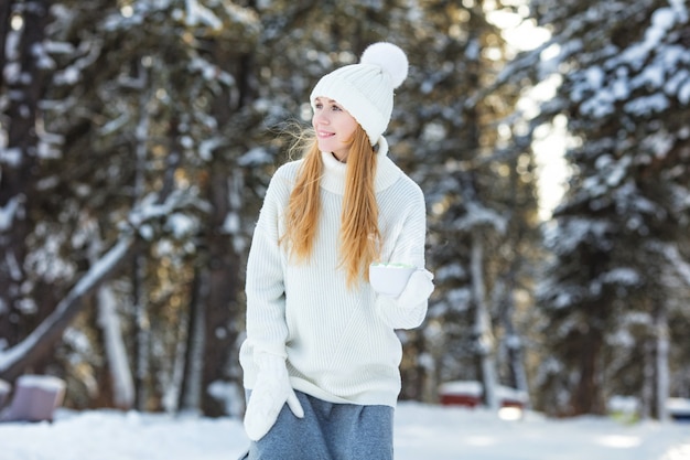 Young adult beautiful woman with coffee mug with marshmallow in hand on nature in winter