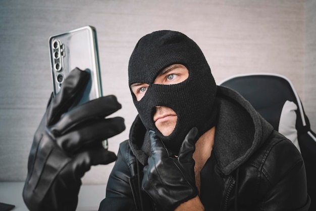 Young adult in black clothes with hidden face Illintended fraudster uses mobile Fraudster calls Scam Mobile racket Hacker hijacks by phone Cellphone account fraud