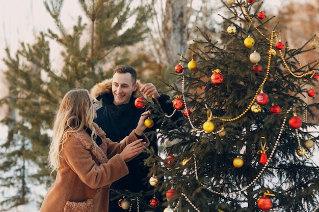 Young adult couple decorates christmas tree in winter forest New year pine holiday party celebration concept