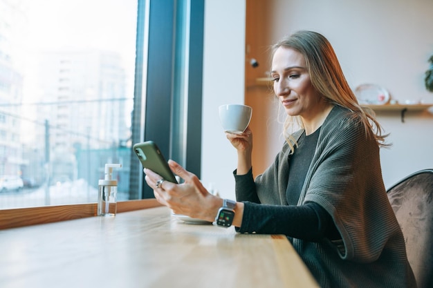 Young adult forty years blonde woman in casual clothes drinking coffee using mobile at the cafe