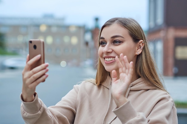 Young adult girl in a beige sweatshirt talking on a mobile phone on a video call