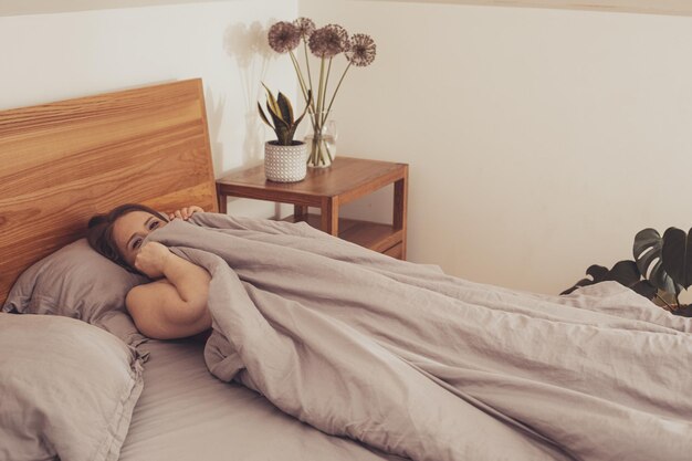 Young adult girl hiding in bed under blanket