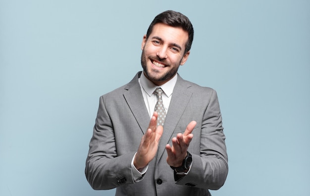 Young adult handsome businessman feeling happy and successful, smiling and clapping hands, saying congratulations with an applause