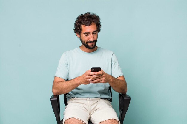 Young adult hispanic crazy man using his phone sitting on a chair