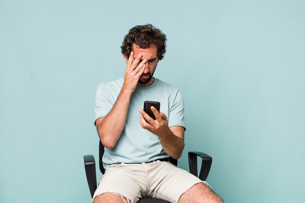 Young adult hispanic crazy man using his phone sitting on a chair