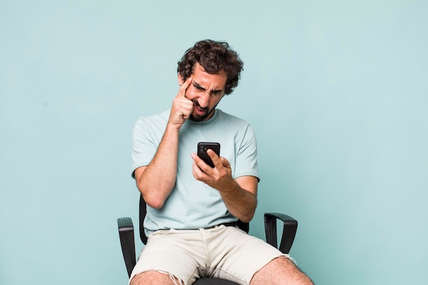 Young adult hispanic crazy man using his phone sitting on a chair