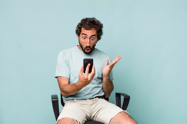 Young adult hispanic crazy man using his phone sitting on a chair