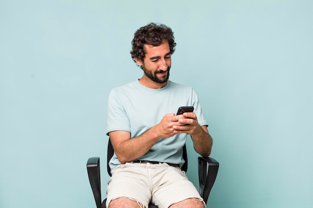 Young adult hispanic crazy man using his phone sitting on a chair