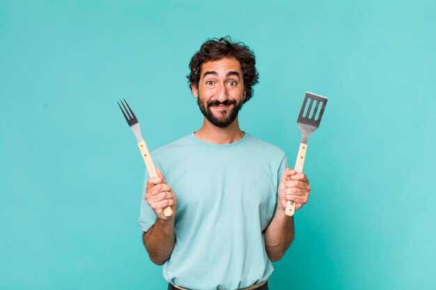 Young adult hispanic crazy man with barbecue tools