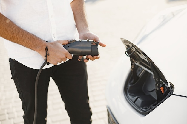 Young adult man charging his electric car in the city. Eco electric car concept.