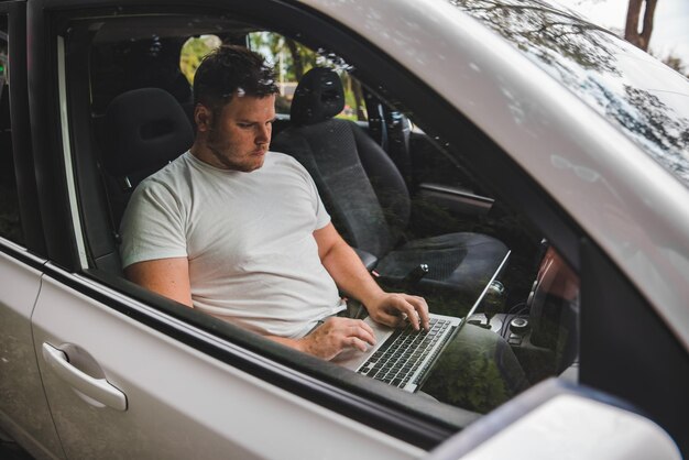 Photo young adult man working in car on laptop