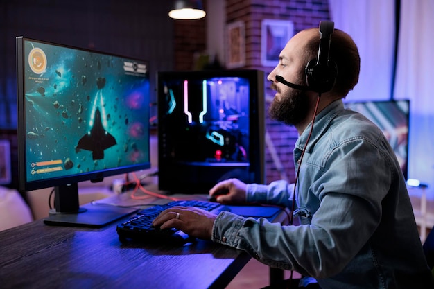 Young adult playing action shooting video games competition in living room with neon lights. Male player streaming live rpg gameplay tournament on computer, enjoying shooter play.