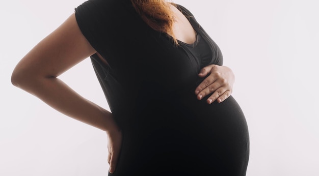 Young adult pregnant woman in white clothes touching big naked belly with hands Showing shape Pregnancy concept Expectation time Closeup Isolated on light gray wall background