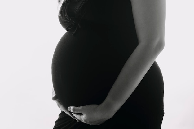 Young adult pregnant woman in white clothes touching big naked belly with hands Showing shape Pregnancy concept Expectation time Closeup Isolated on light gray wall background