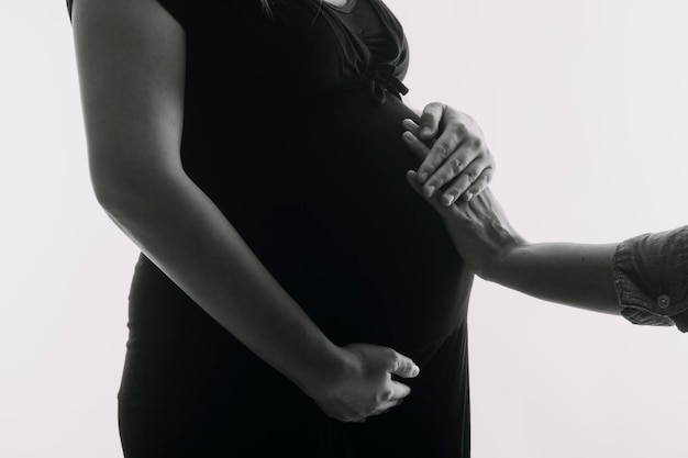 Young adult pregnant woman in white clothes touching big naked belly with hands Showing shape Pregnancy concept Expectation time Closeup Isolated on light gray wall background