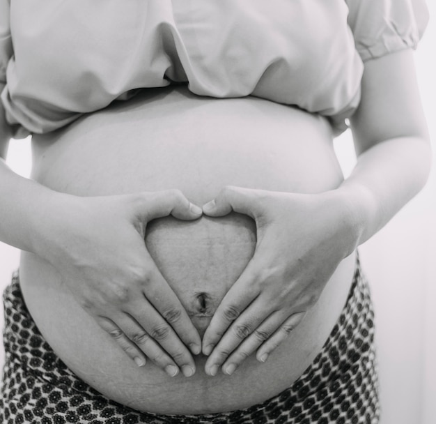 Young adult pregnant woman in white clothes touching big naked belly with hands Showing shape Pregnancy concept Expectation time Closeup Isolated on light gray wall background