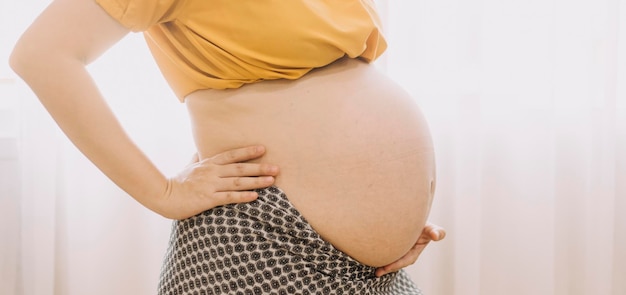 Young adult pregnant woman in white clothes touching big naked belly with hands Showing shape Pregnancy concept Expectation time Closeup Isolated on light gray wall background