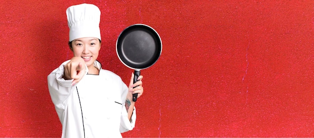 Young adult pretty asian woman restaurant chef with a frying pan