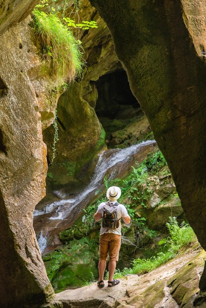 Young adult strong man with backpack at cave entrance looking on sunlight