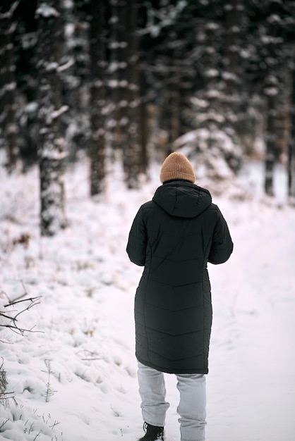 Young adult woman alone slowly walking after snowfall Peaceful atmosphere in winter day Enjoying fresh air in park Back view