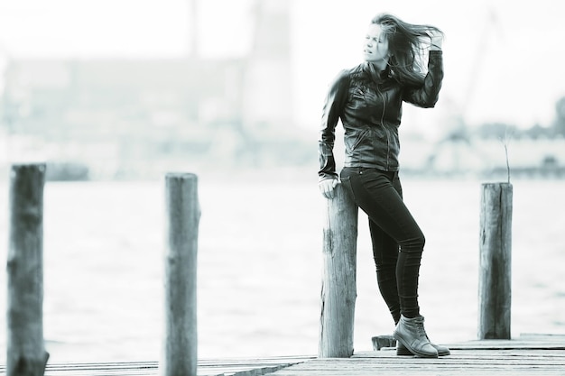 Young adult woman sitting on a wooden jetty on the river