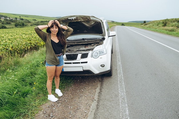 Young adult woman standing near broken car on highway and talkin