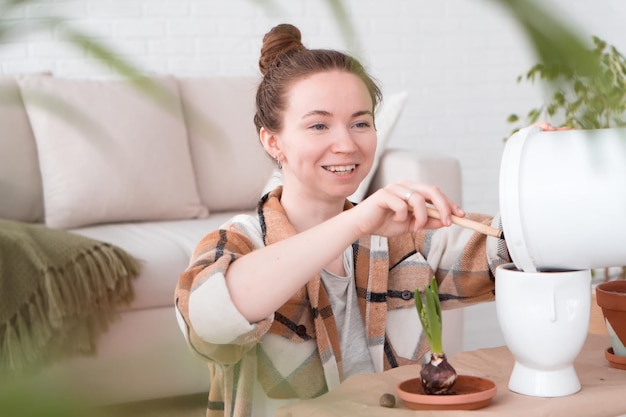 Young adult woman transplanting plants to new pots at home sitting on floor