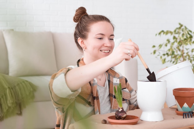 Young adult woman transplanting plants to new pots at home sitting on floor