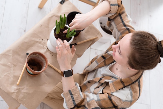 Young adult woman transplanting plants to new pots at home sitting on floor