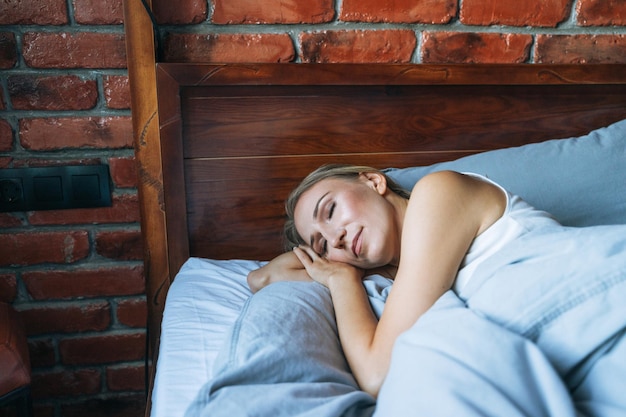 Young adult woman with blonde long hair sleeping on bed in loft room at the home