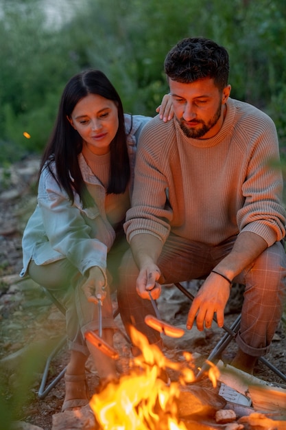 Young affectionate couple frying sausages over fire