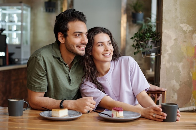 Young affectionate couple looking through window while sitting by table in cafe