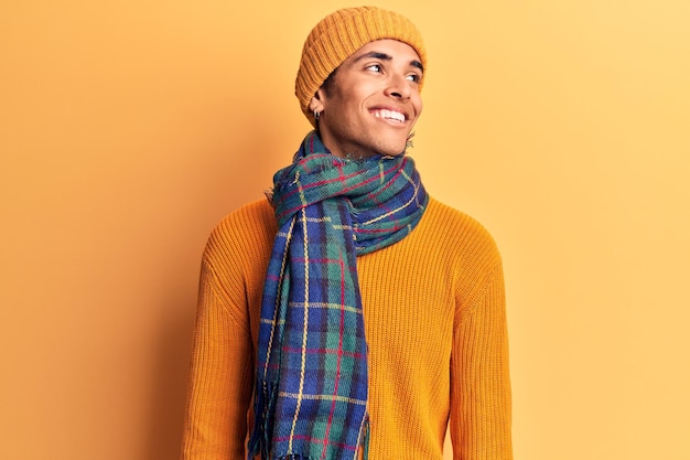 Young african amercian man wearing casual winter clothes looking away to side with smile on face, natural expression. laughing confident.