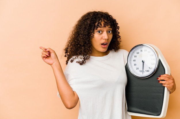 Young african american afro woman holding a scale pointing to the side