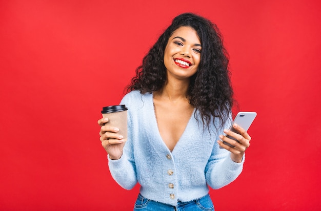 young african american black woman holding a coffee cup and mobile phone isolated over red background