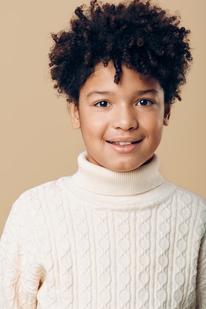 Photo a young african american boy with curly hair wearing a white turtleneck and smiling playfully against a neutral background