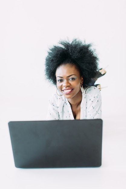 Young african american business woman using the laptop, while lying on the floor, isolated